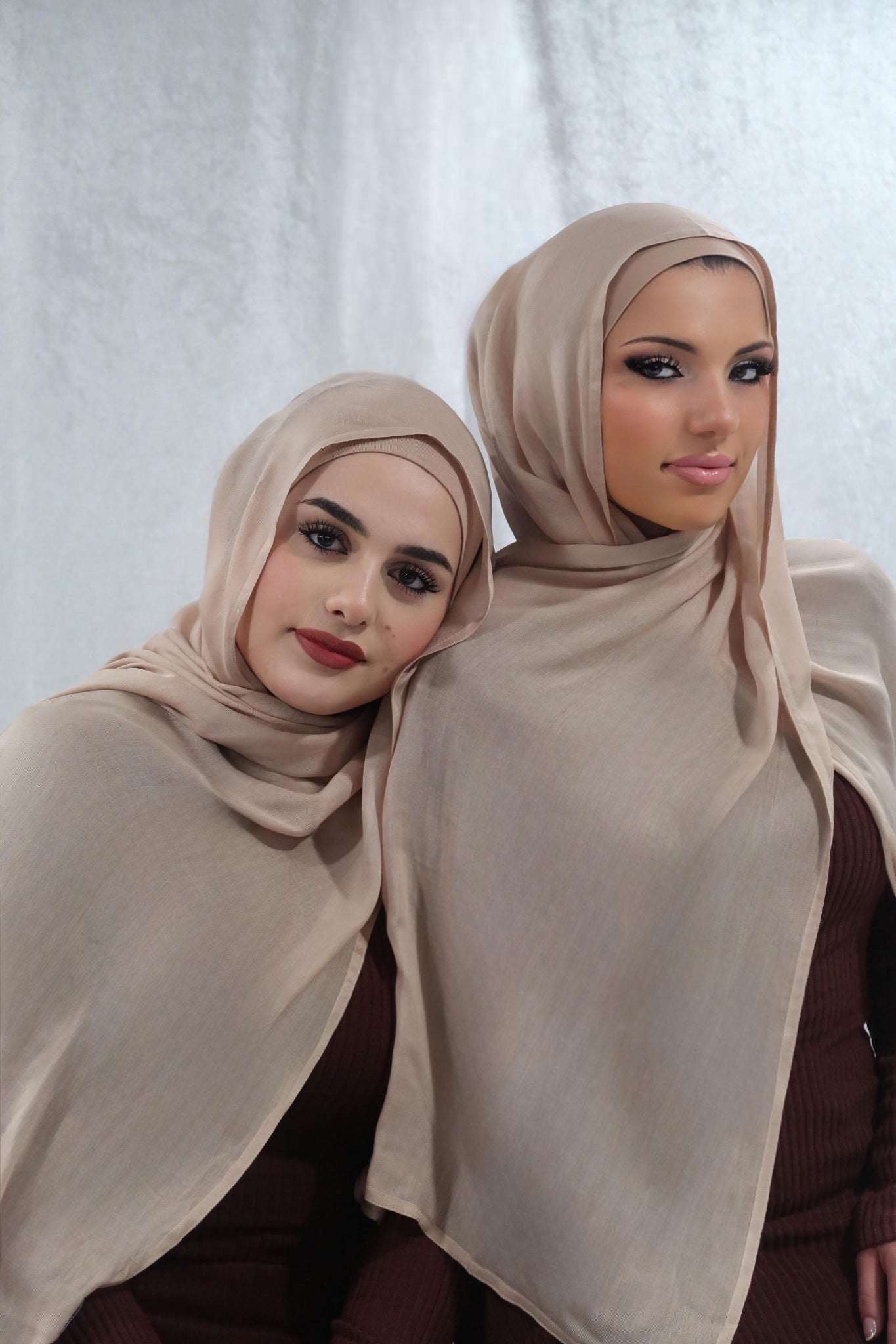Two women wearing beige hijabs against a white background